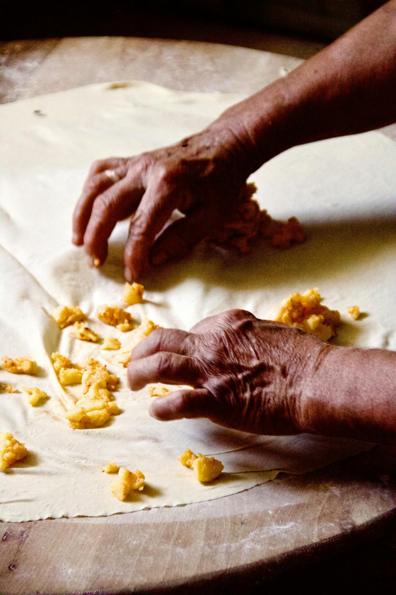 Close-up of hands rolling dough with apple filling on a wooden table, perfect for homemade baking themes.