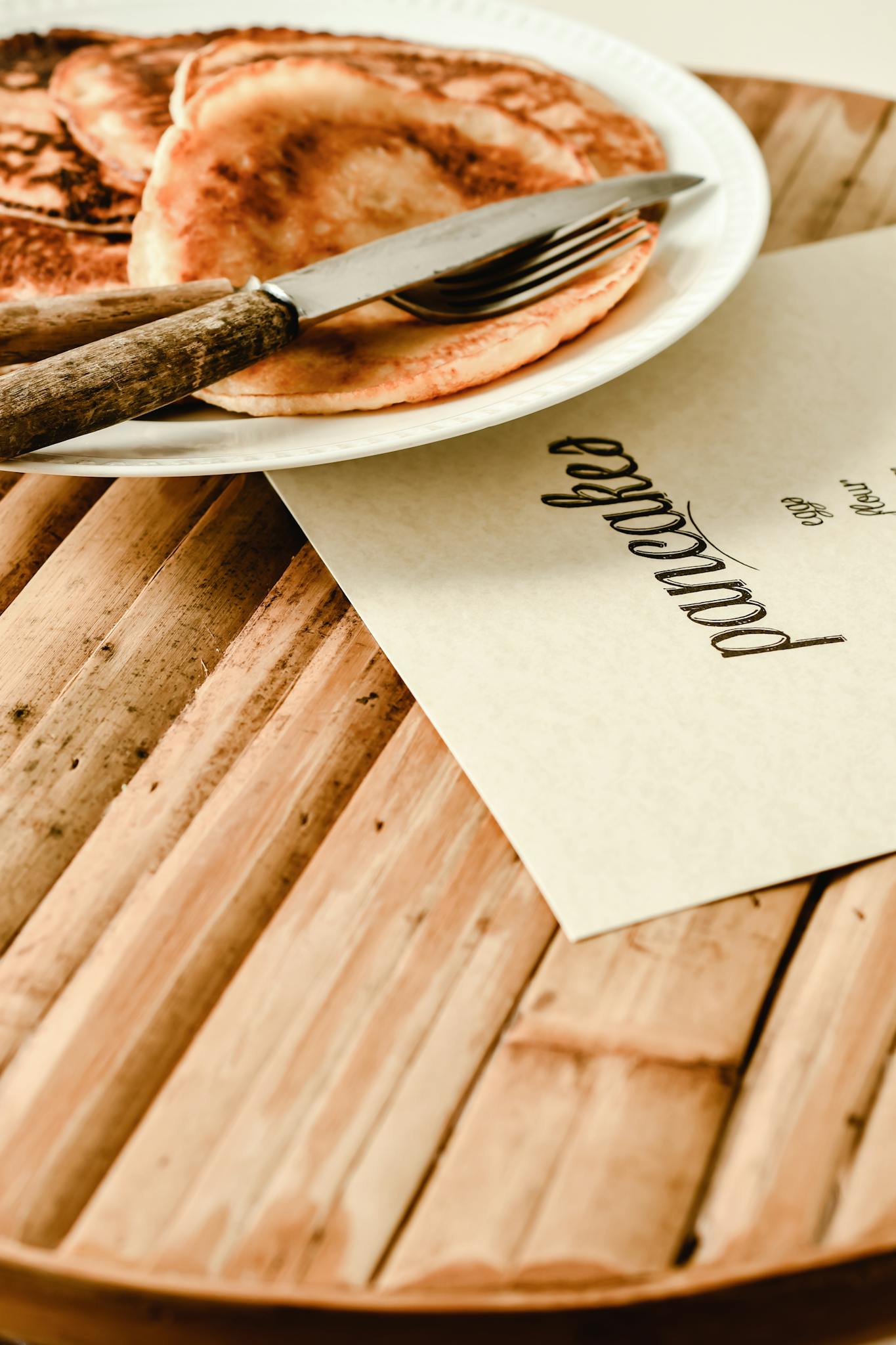 Close-up of pancakes on a wooden table with a fork and knife, creating a cozy breakfast scene.